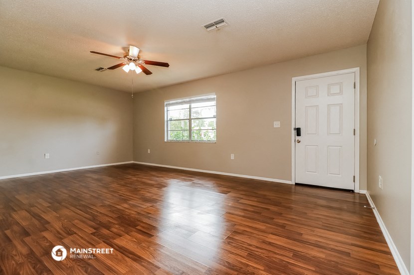 an empty living room with a ceiling fan and a white door