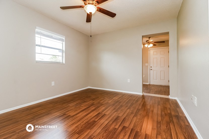 the spacious living room with hardwood flooring and a ceiling fan