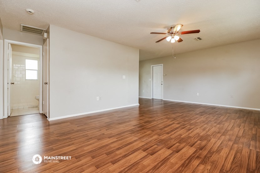 the spacious living room with hardwood flooring and a ceiling fan