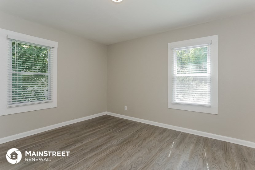 the interior of an empty room with wooden floors and two windows
