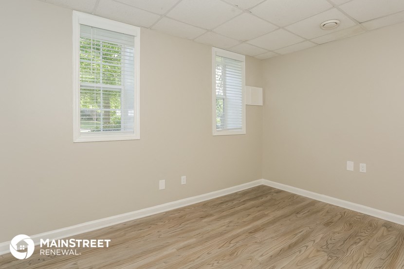 the interior of an empty room with wood flooring and two windows