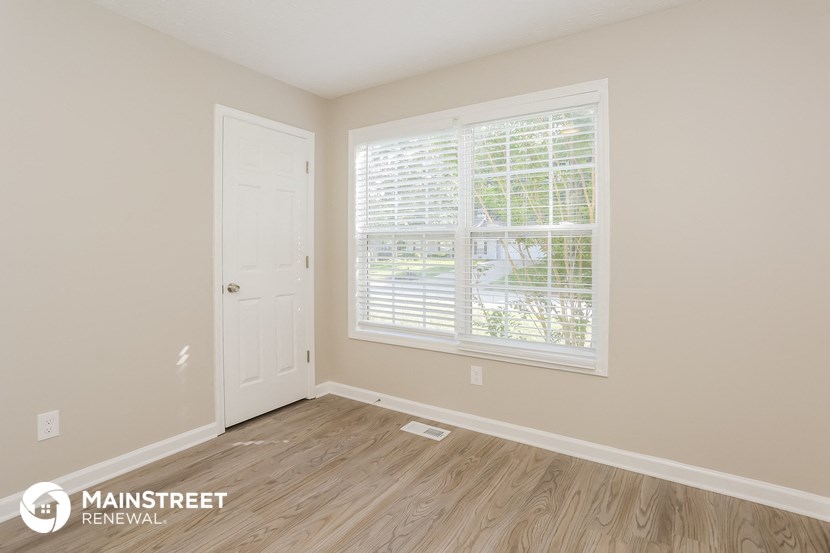 the living room of a home with a large window and wooden floors