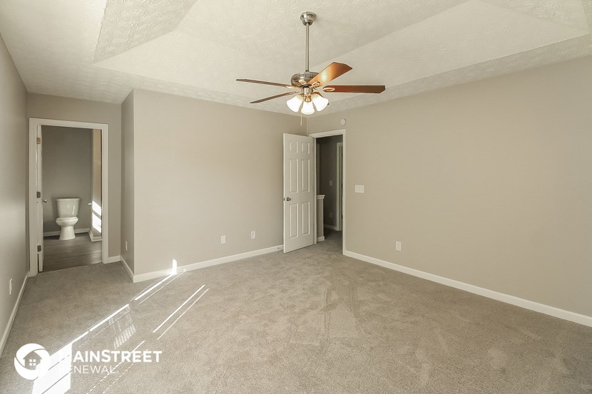 an empty living room with a ceiling fan and a door to the bathroom