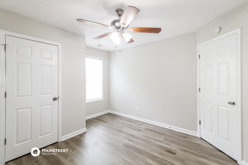 the spacious living room with white walls and a ceiling fan