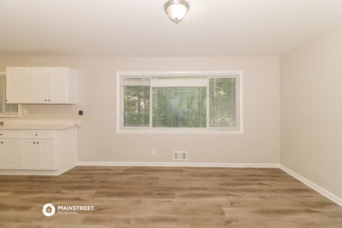 the living room and kitchen of a house with white cabinets and a window