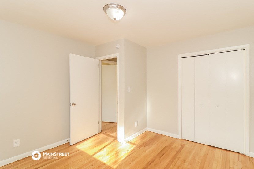 a bedroom with white walls and wood floors and a closet