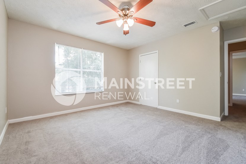 an empty living room with a large window and a ceiling fan