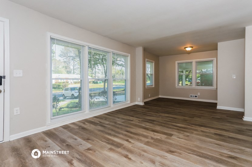 the living room of a house with wood flooring and large windows