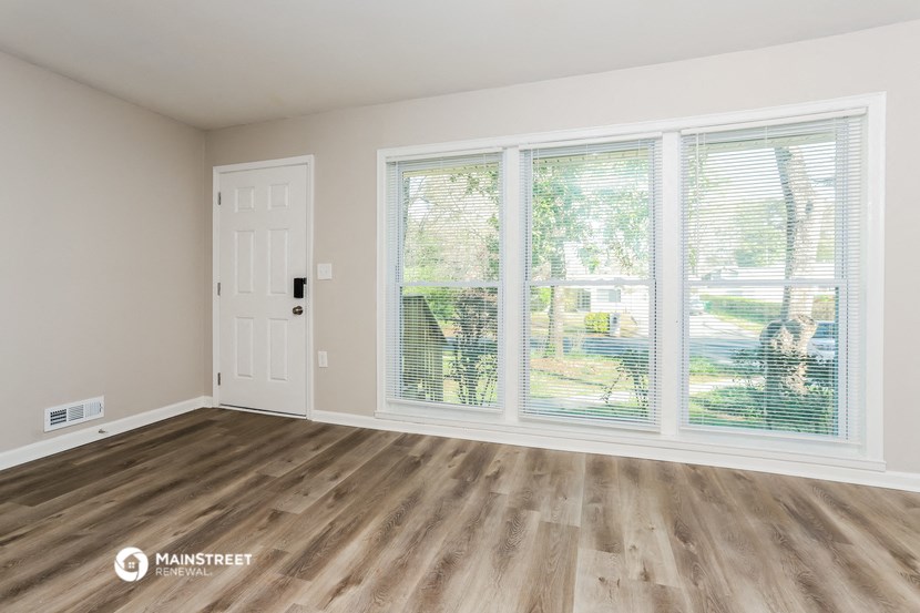 the living room of a home with a large window and wood floors