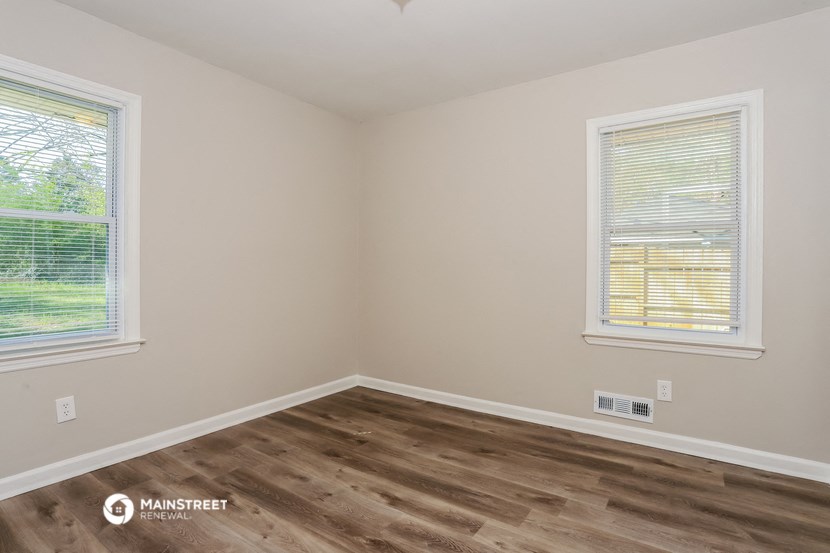 the living room of a house with wooden floors and two windows