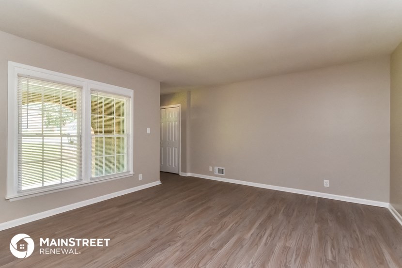 the living room of an apartment with wood flooring and a large window