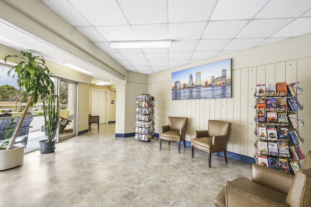 Sitting area with large windows and towers of paperback books for residents to enjoy