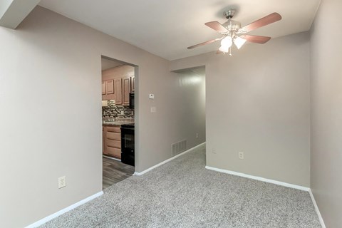 an empty living room with a ceiling fan and a kitchen