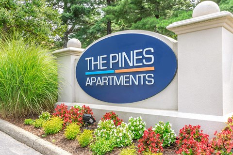 the pines apartments sign in front of plants and flowers