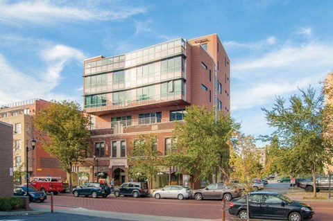 A modern building with a glass facade is situated on a street with cars parked on the side.
