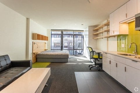 A modern office space with a black leather sofa, a green chair, and a kitchenette.