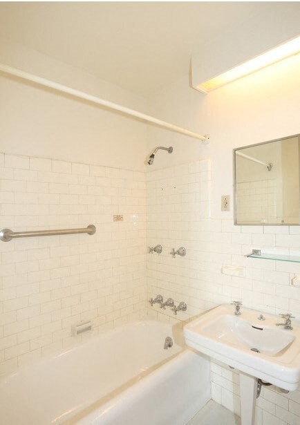 A white bathroom with a white tub, sink, and tiles.