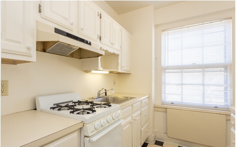 A white kitchen with a stove and a window.