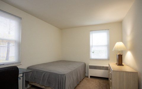 A bedroom with a bed, a chair, a nightstand, and a window.