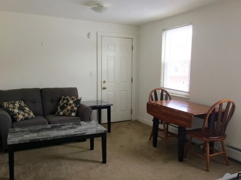 A living room with a grey couch, a wooden table and two chairs.