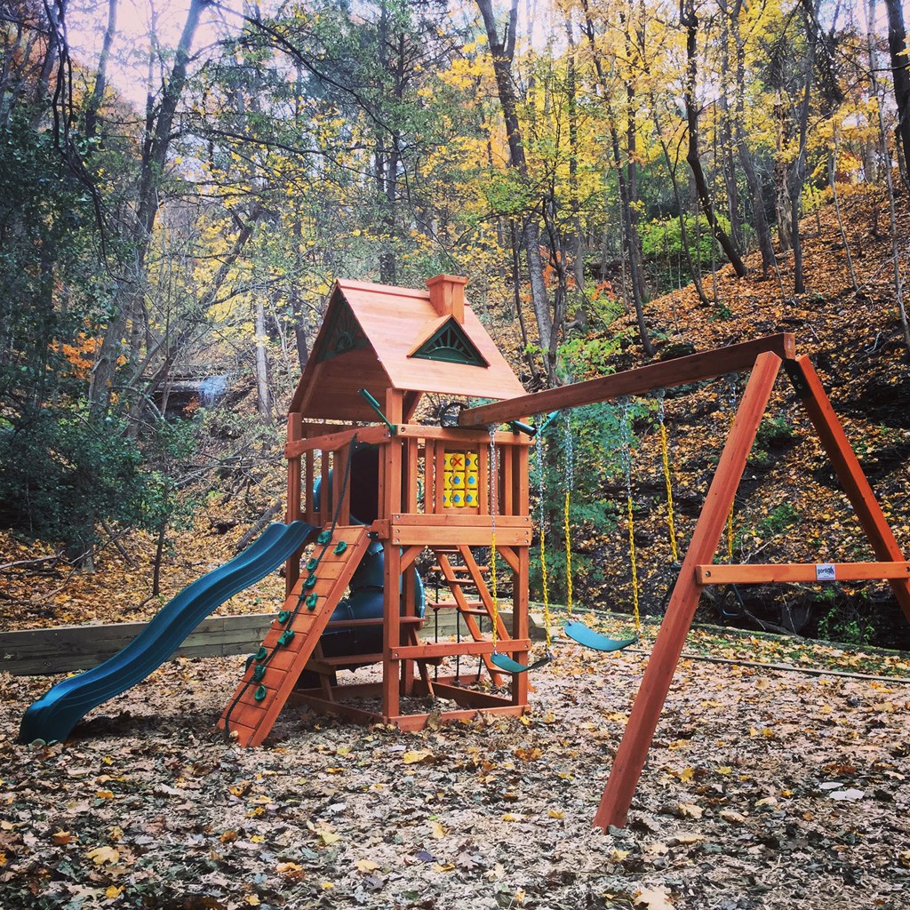 a wooden swing set in the middle of the woods