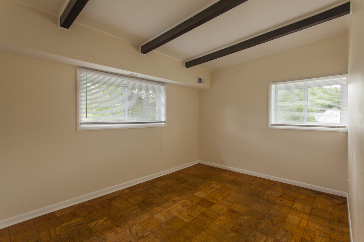 a bedroom with wood floors and two windows