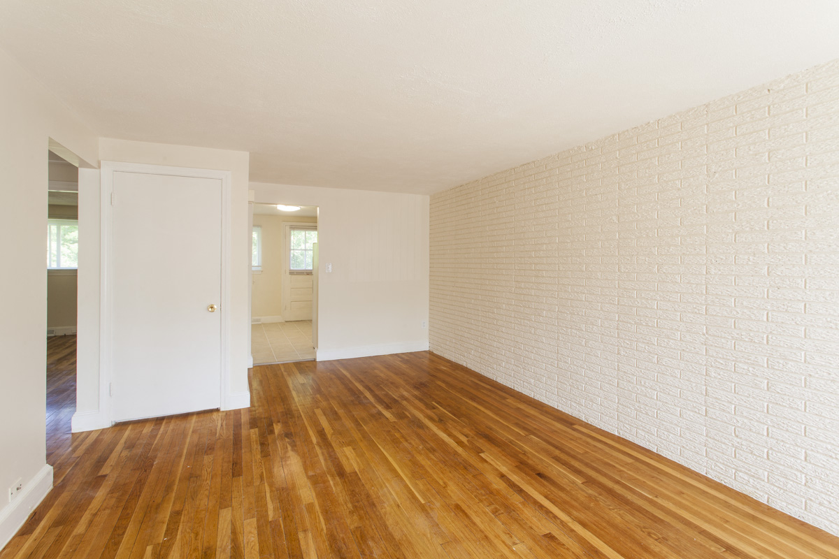 an empty living room with wood floors and a white brick wall