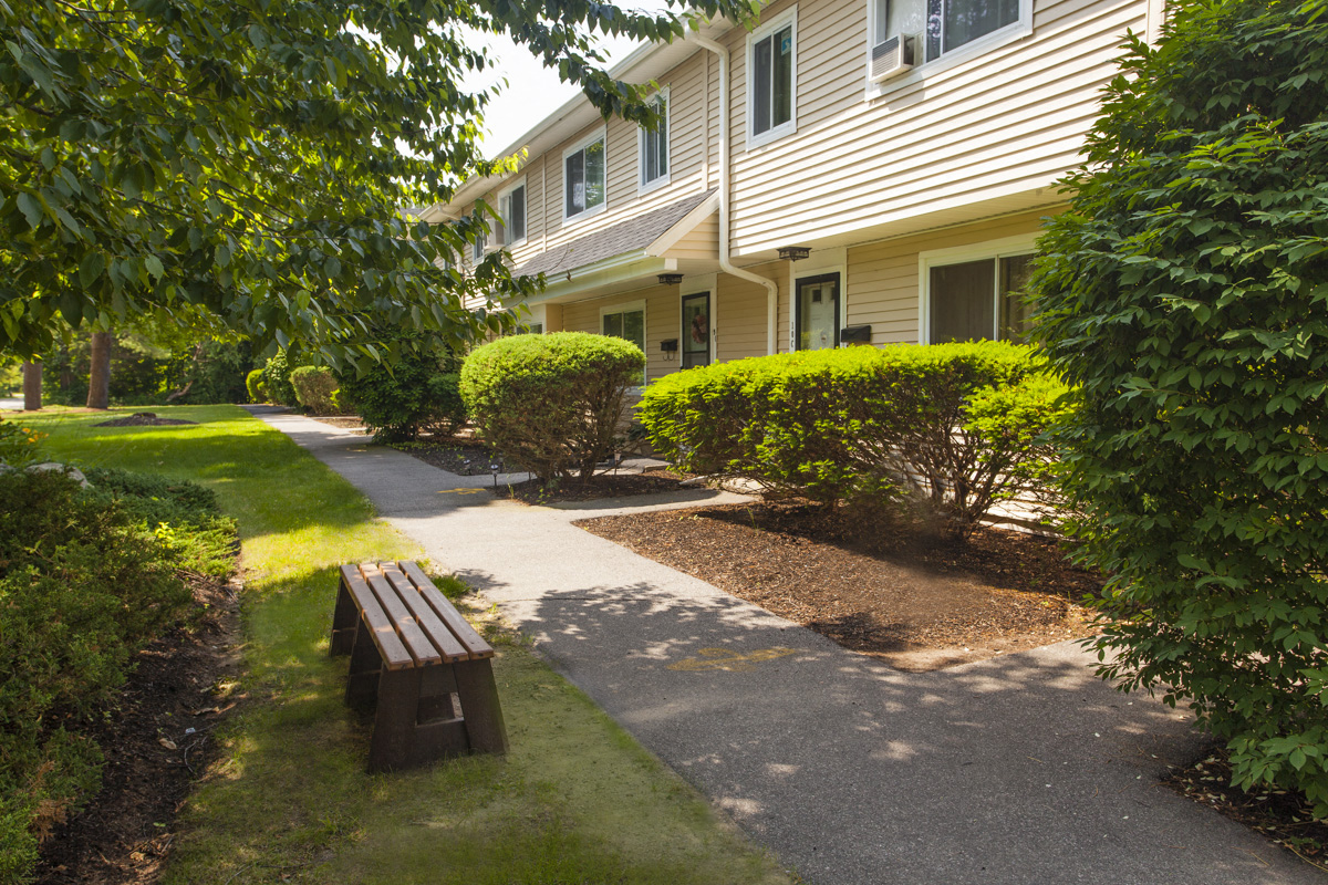 a walkway with a bench in front of a house