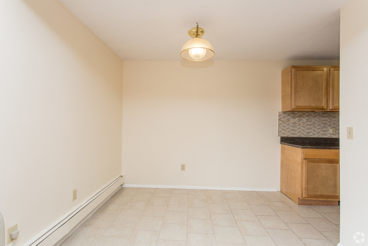 an empty living room with a kitchen with cabinets and a ceiling lamp