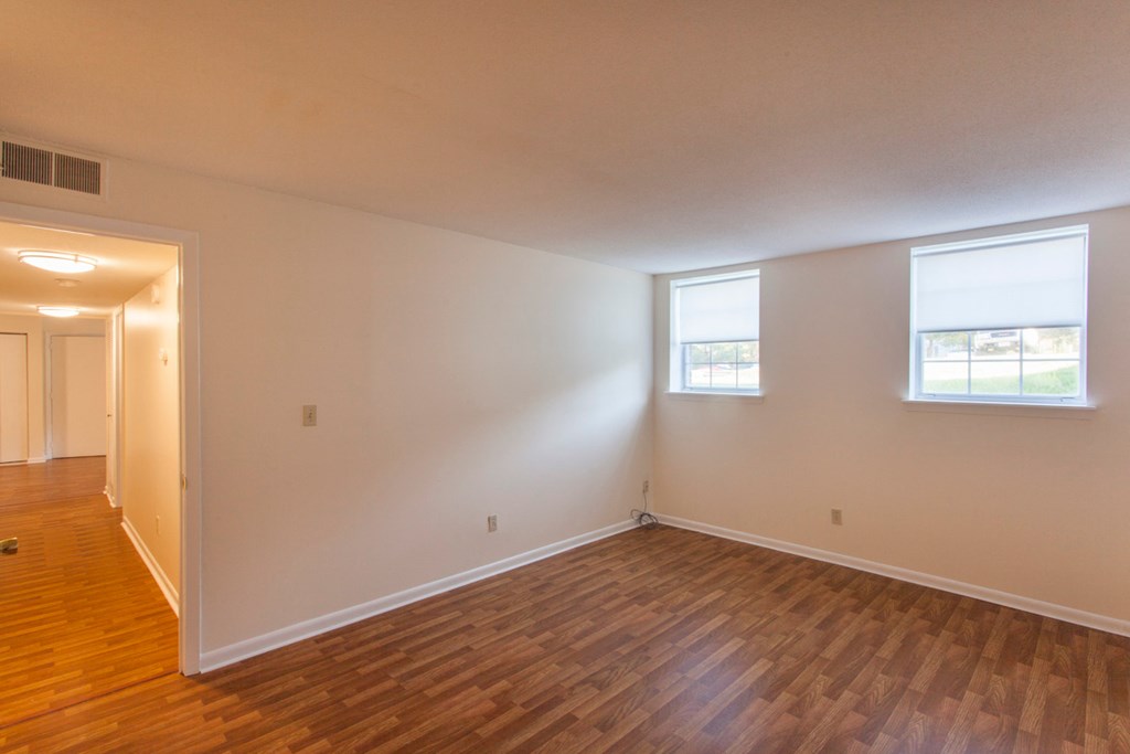 the living room and dining room of an empty house with wooden floors and two windows