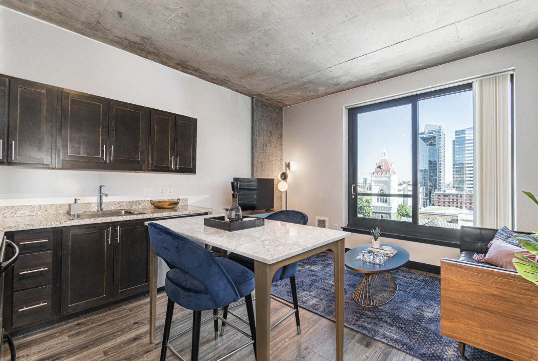 a living room with a large window and a kitchen with a table and chairs