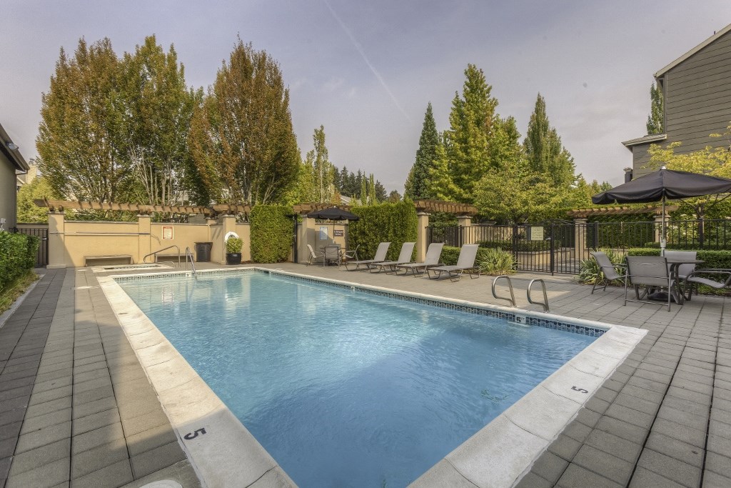a pool with chairs and umbrellas in a backyard with trees