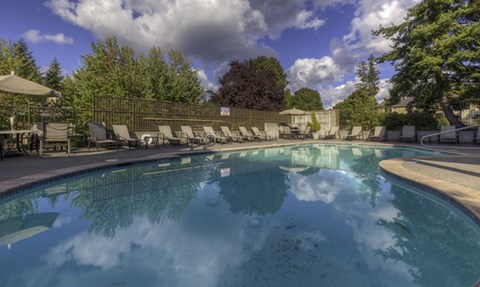 a swimming pool with chairs and umbrellas and a cloudy sky