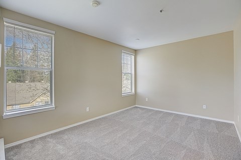 an empty living room with two windows and carpeting