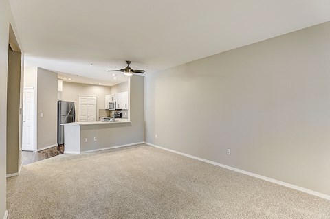 an empty living room with a kitchen in the background