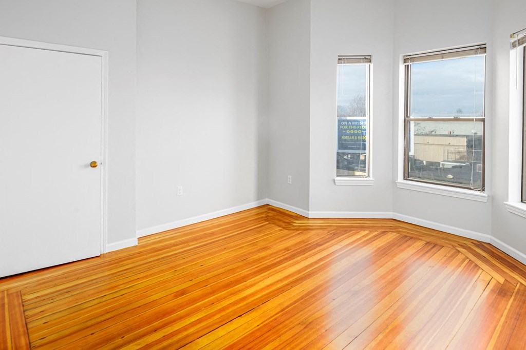 an empty room with wood floors and three windows