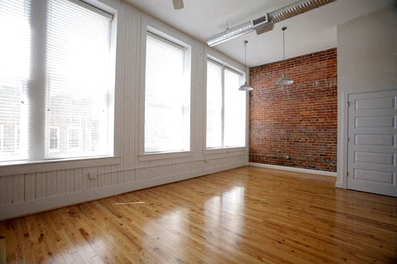 an empty living room with a brick wall and wood floors