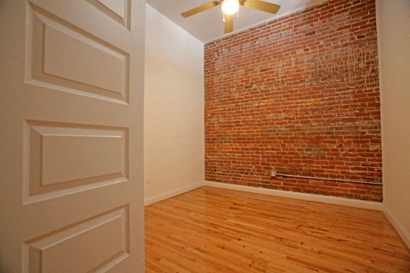 an empty room with a brick wall and a ceiling fan