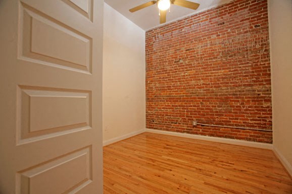 a room with a brick wall and wooden floors and a ceiling fan