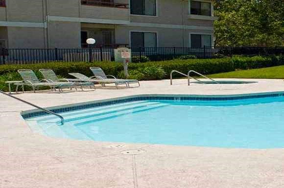 a large swimming pool with lawn chairs and a building in the background