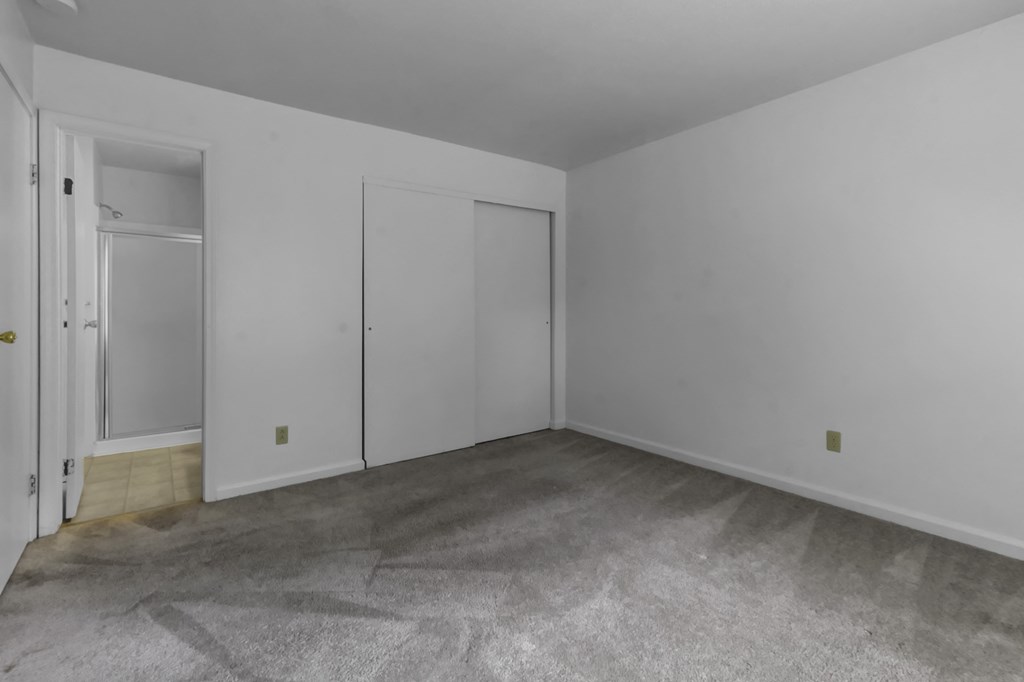 a living room with white walls and carpet and a door to a closet