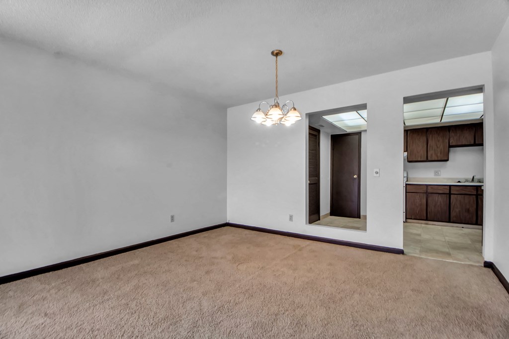 A room with a brown carpet and a chandelier hanging from the ceiling.