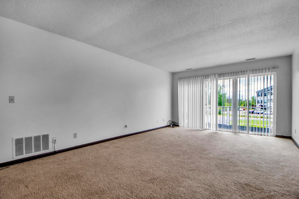 A room with a carpeted floor and a window with blinds.