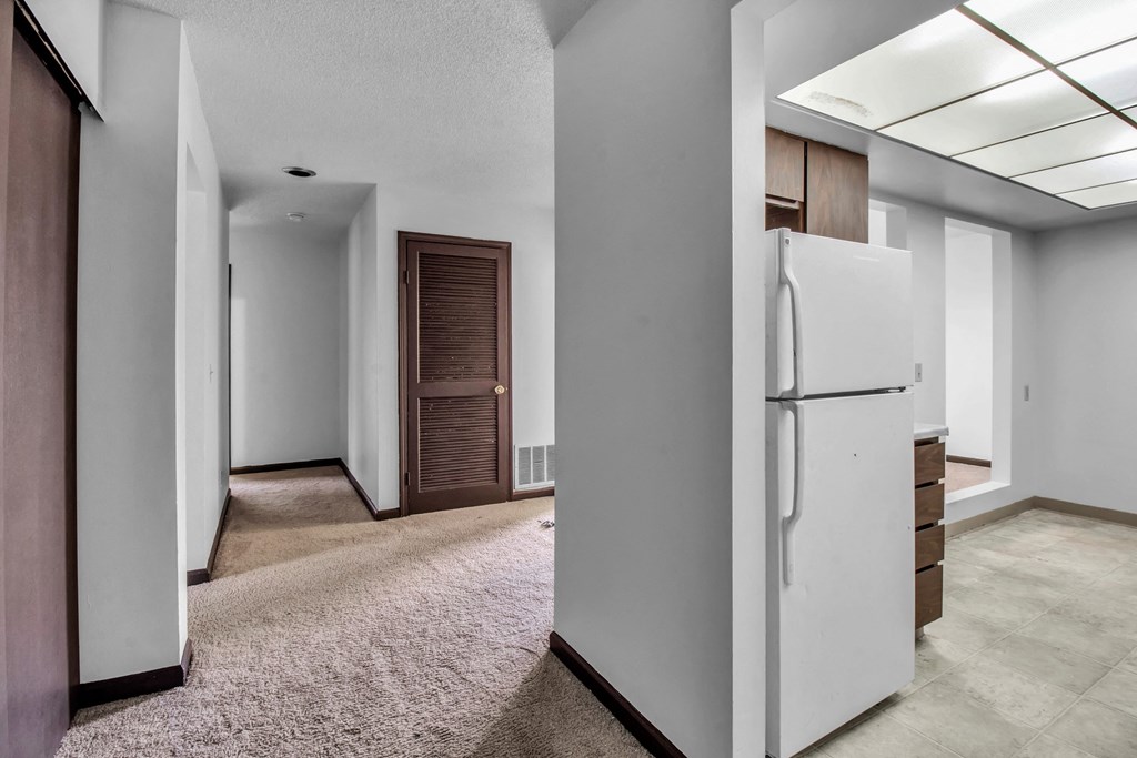A white refrigerator is in a kitchen with a brown door.