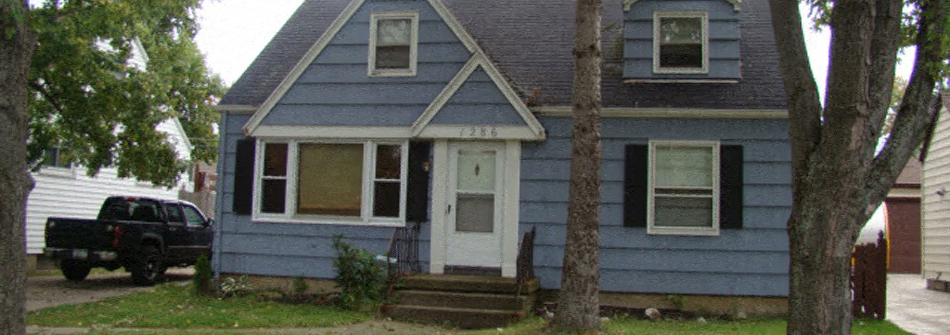 A blue house with a white door and a truck parked in front.