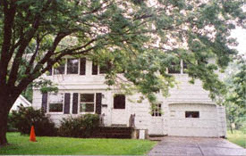 A white house with a black roof and a white fence.