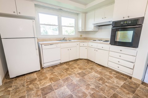 A kitchen with white appliances and brown tiled floors.