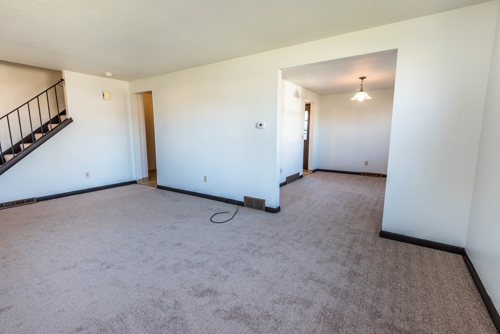 an empty living room with white walls and carpet and a staircase