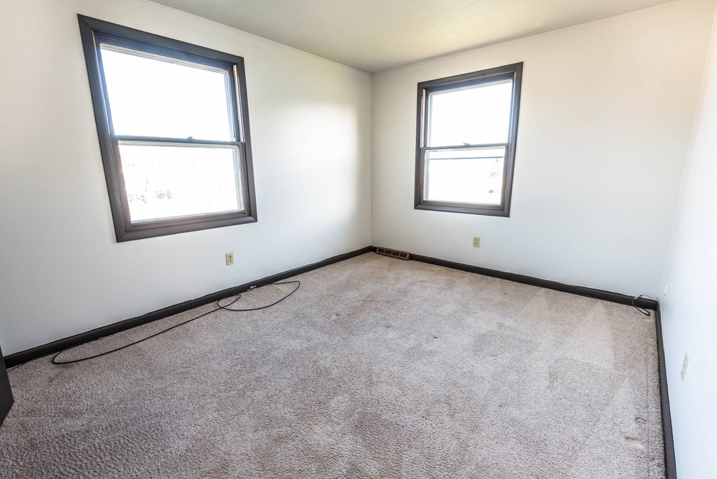 an empty room with two windows and a carpeted floor