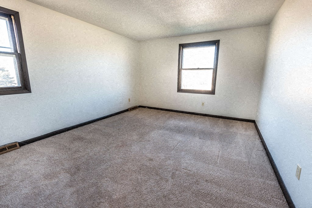 a room with a carpeted floor and two windows
